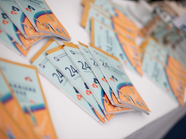 Mehrere bunte Broschüren mit der Aufschrift '24 Karrieremesse' und Regenbogengrafik, ordentlich auf einem weißen Tisch ausgelegt.