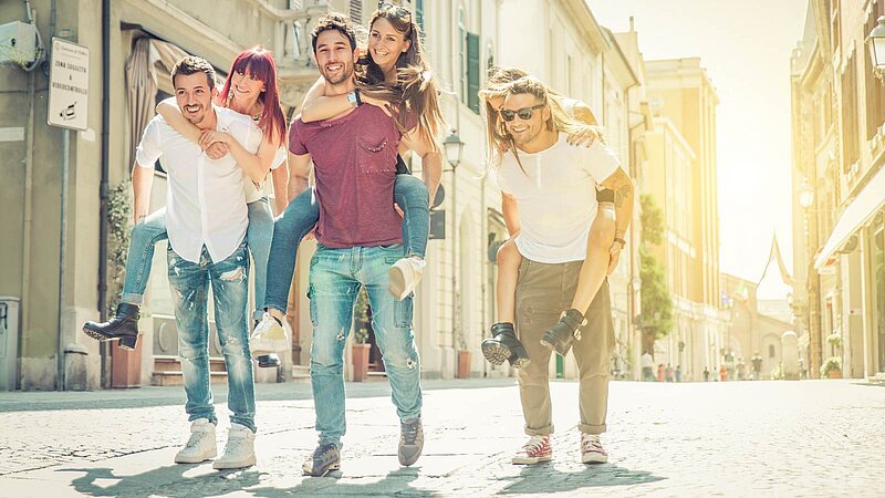 3 Menschen auf drei Menschen rennen Huckepack nebeneinander auf einer Straße